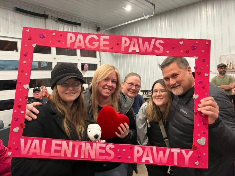 Five people holding up and standing behind a red rectangular frame that says "Page Paws Valentines Pawty"